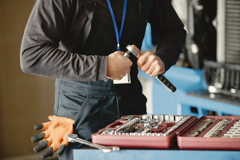 Mechanik trzyma klucz dynamometryczny, obok stoi otwarta czerwona walizka z nasadkami